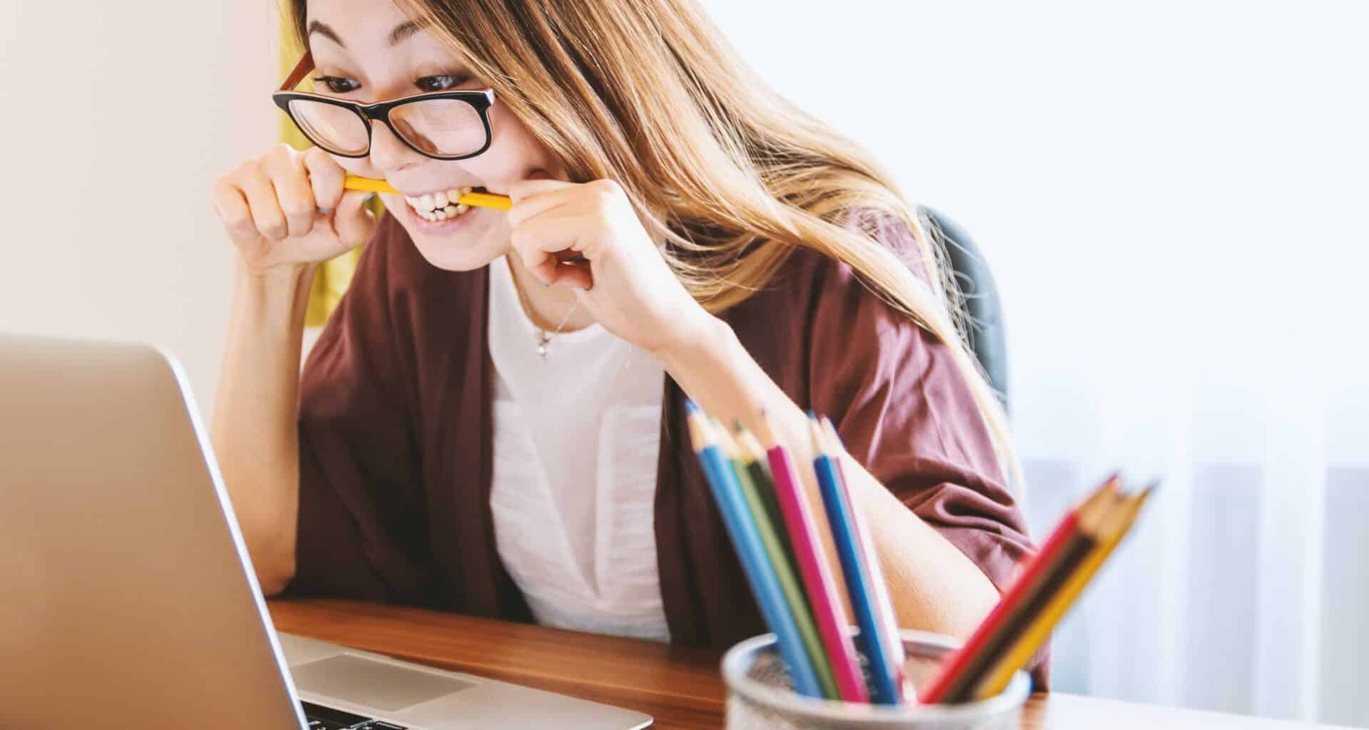 Jovem segurando lápis com a boca enquanto olha para computador