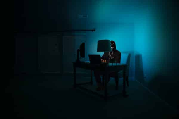 Pessoa sentada na frente de um computador em uma sala secreta representado uma equipe de hackers.