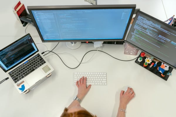 Pessoa programando com um computador e duas telas.