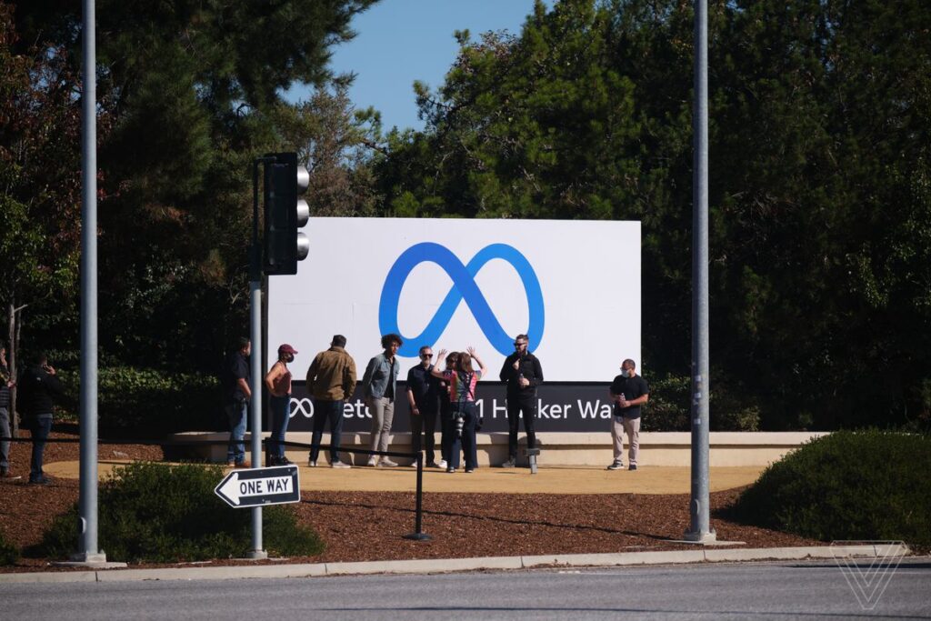 Pessoas interagindo entre si em frente a um outdoor com a logo da empresa Meta