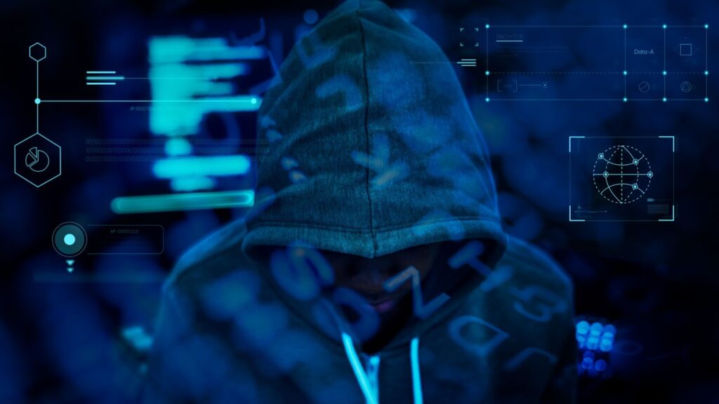 Imagem ilustrativa de hacker, usando elementos da computação em um fundo azul. No centro, uma pessoa usando blusa de capuz, cobrindo a maior parte do rosto.