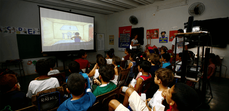 Grupo de crianças assistindo a um filme em um telão em sala de aula